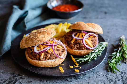 Two homemade sloppy joes on toasted buns topped with cheddar and red onion, served with fries and a bowl of spicy ketchup