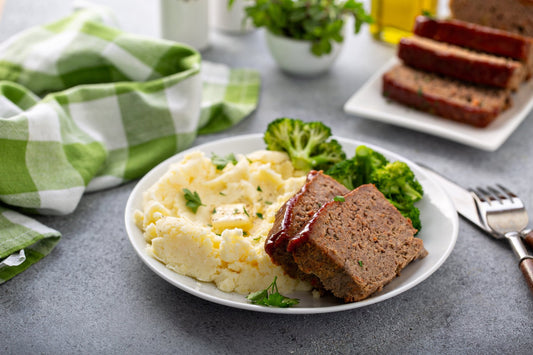 Sliced ketchup glazed meatloaf on a white plate with mashed potatoes and broccoli
