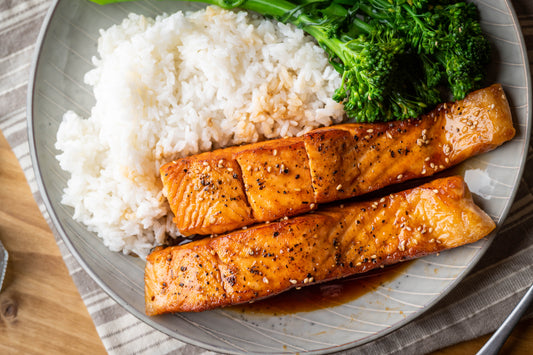 Two glossy glazed salmon fillets served with white rice and broccolini on a plate