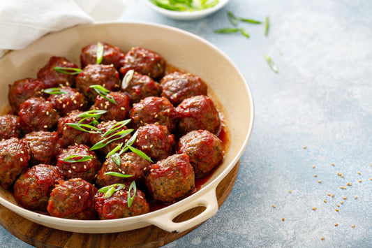Sweet and spicy meatballs coated in a glossy sticky glaze in a cream skillet, topped with sliced scallions and sesame seeds